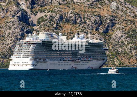 4 juillet 2026, Kotor, Monténégro, navire de croisière blanc ancré à côté de falaises rocheuses escarpées dans une mer bleue calme, petite embarcation de service au premier plan sous un éclairage vif Banque D'Images