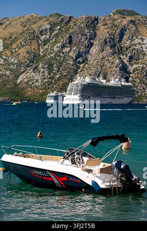 4 juillet 2026, Kotor, Monténégro, un navire de croisière est ancré près de falaises abruptes tandis qu’un petit bateau à moteur repose dans les eaux calmes de l’avant-plan, soleil éclatant de midi Banque D'Images