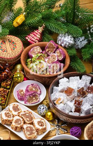 Grossissement vertical de divers loukoums turcs aux noix et au sucre en poudre présentés dans des bols en céramique avec des pommes de pin et des ornements de Noël festifs Banque D'Images