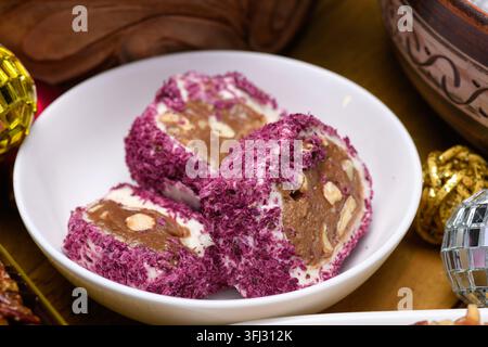 Rouleaux de délicatesse turque premium avec noix et copeaux de noix de coco violets servis dans un bol en céramique blanche. Banque D'Images