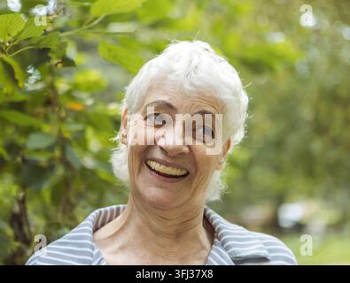 Portrait d'une femme âgée souriante dans un parc. Portrait en gros plan. Femme mûre heureuse et pensive se détendant en plein air. Banque D'Images