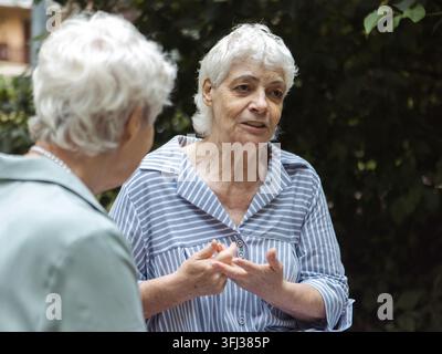 Deux amies âgées sont assises sur un banc et discutent par une journée d'été. Banque D'Images