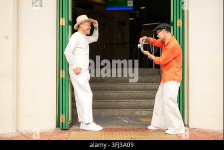 Voyageur LGBTQ senior prenant des photos de son partenaire à l'entrée d'un bâtiment historique à Bangkok, Thaïlande. Voyages de retraite, photographie et cul… Banque D'Images