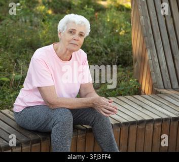 Ancienne femme souriante assise sur un banc en bois dans le parc en été Banque D'Images