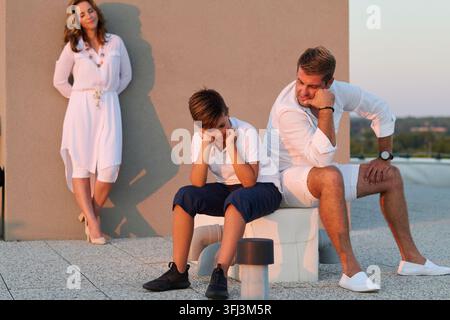 Famille Père et fils dans un moment tendu sur le balcon du toit avec la mère qui observe Banque D'Images