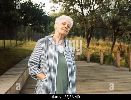 Une femme âgée aux cheveux courts et bouclés marche dans un parc en été. Banque D'Images