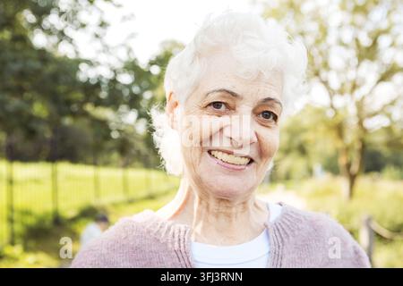 Portrait d'une femme âgée souriante dans un parc. Portrait en gros plan. Femme mûre heureuse et pensive se détendant en plein air. Banque D'Images