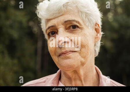 Portrait d'une femme âgée souriante dans un parc. Portrait en gros plan. Femme mûre heureuse et pensive se détendant en plein air. Banque D'Images