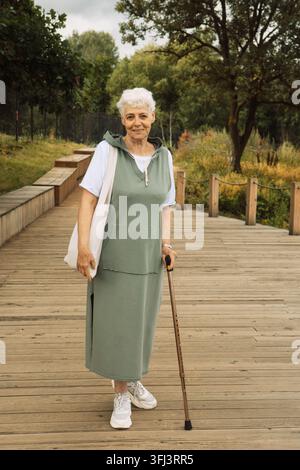 Une femme âgée avec une canne marche dans un parc en été. Banque D'Images