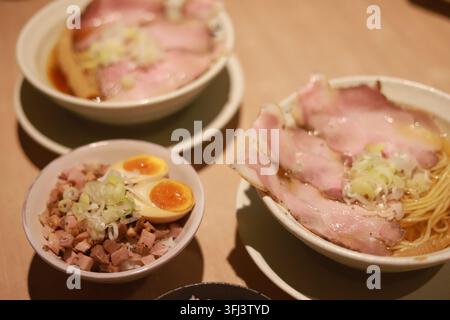 Grossissement de deux bols de nouilles ramen japonaises avec des tranches de porc et un plat d'accompagnement de riz au porc sur une table en bois Banque D'Images
