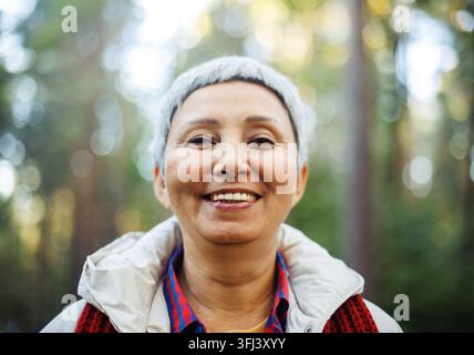 Femme asiatique âgée souriante aux cheveux gris courts dans le parc. Banque D'Images