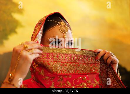 Jeune modèle hindoue avec des bijoux traditionnels. Costume indien en saree rouge. Une femme indienne ou musulmane couvre son visage. Banque D'Images