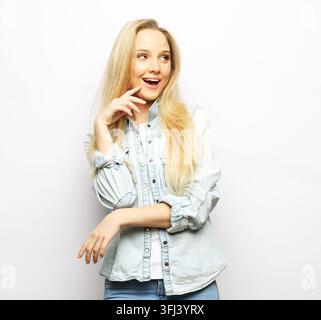 Jeune femme aux longs cheveux blonds portant une chemise en jean décontractée souriant sur fond blanc Banque D'Images