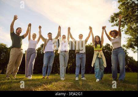 Amis divers se tenant par la main dans un parc, célébrant l'unité, le travail d'équipe et la communauté Banque D'Images