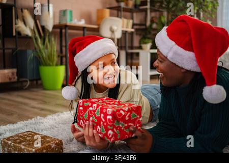 Mère offrant un cadeau de Noël à sa fille heureuse portant un chapeau du Père Noël Banque D'Images