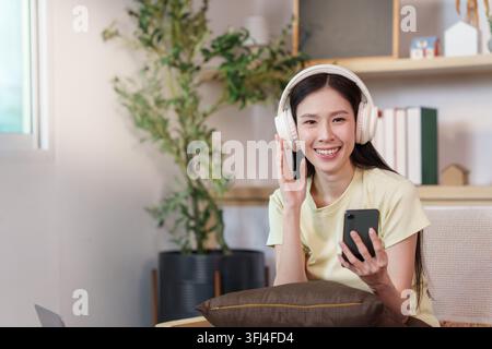 Femme asiatique utilisant un smartphone et des écouteurs pour écouter une application mobile à la maison Banque D'Images