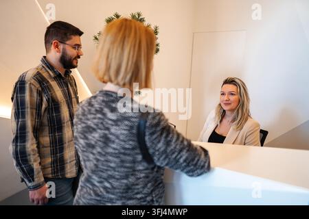 Clients interagissant avec la réceptionniste au bureau moderne de réception Banque D'Images