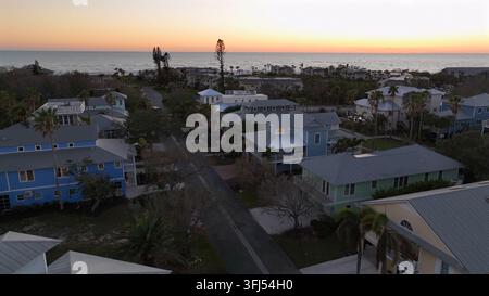 Plan aérien ascendant d'un coucher de soleil serein sur Longboat Key, FL. Maisons charmantes alignées le long d'une rue tranquille avec des palmiers. Atmosphère paisible au coucher du soleil. Banque D'Images