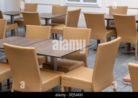 Des chaises tissées vides et des tables sont disposées sur une terrasse de café extérieure tranquille. Banque D'Images