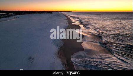 Plage enneigée au lever du soleil. Les vagues de l'océan s'écrasent sur le rivage. Plage de sable enneigée au coucher du soleil. Vue aérienne par drone, Jackson Township, New Jersey. Banque D'Images