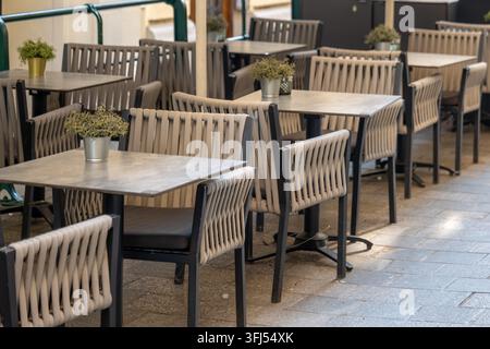 Terrasse de café moderne vide avec des chaises tressées, des tables carrées et de petites plantes en pot. Banque D'Images