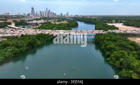 Paddleurs sur la rivière Colorado avec panorama de la skyline d’Austin Texas au loin. Des voitures circulent sur le pont. Vue aérienne. Banque D'Images