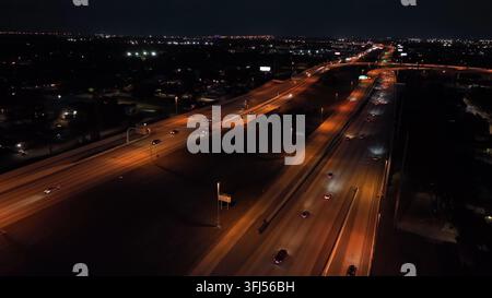 Autoroute illuminée en orange en Floride avec un trafic intense de nuit. Plan aérien de survol. De nombreuses voitures roulent à toute allure sur la route à minuit. Tam Banque D'Images