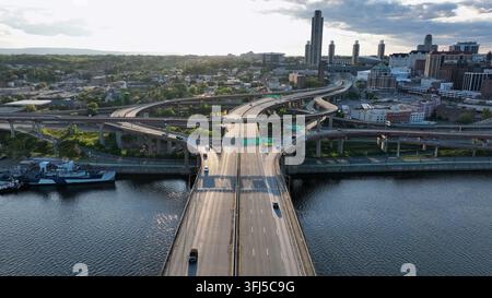 Conduire des voitures sur le pont commémoratif Dunn menant au centre-ville d'Albany, New York. Coucher de soleil doré paisible dans une ville américaine. Nuages dans le ciel. Plan large aérien Banque D'Images