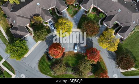Arbres multicolores dans un quartier de banlieue noble avec des villas par une journée d'automne ensoleillée. Prise de vue aérienne de dessus en forme de cercle. Grands terrains et voitures garées en qu Banque D'Images