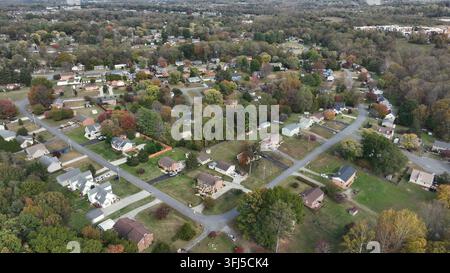 Vue aérienne par drone d'un quartier de banlieue américaine avec un feuillage automnal éclatant, des rues tranquilles, de grands jardins et des bois environnants sous un ciel clair Banque D'Images