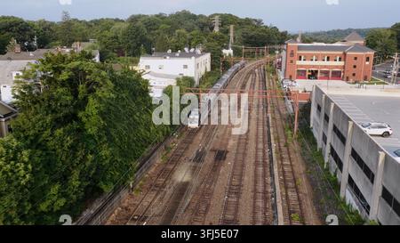 Les voies de train de banlieue s'étendent entre des maisons mitoyennes modernes et un bâtiment de gare en brique à Orange, dans le New Jersey, un parking et une canopée d'arbres denses bordent la ligne Banque D'Images