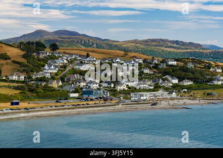 Maisons côtières nichées sur une colline surplombant la mer à Criccieth, dans le nord du Pays de Galles, avec des voitures garées le long de la promenade et des collines verdoyantes s'élevant en arrière-plan Banque D'Images