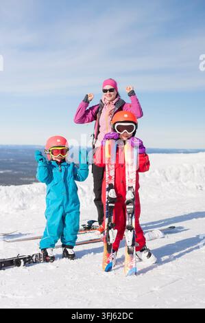 Enfants joyeux et maman posant avec des skis sur une montagne enneigée, exprimant leur enthousiasme, pendant les vacances de Pâques en fin de printemps, Yllaes Ski Resort, K Banque D'Images
