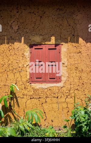 Volets de fenêtre en bois rouges sur un mur de briques en terre cuite fissuré, Y Ty, Lao Cai, Vietnam Banque D'Images