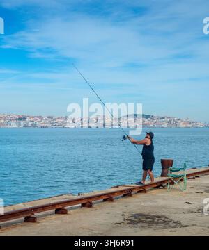 LISBONNE, PORTUGAL - nov 09, 2025 : homme pêchant depuis la jetée de Cais do Sodre sur le Tage, Lisbonne skyline en arrière-plan. Banque D'Images