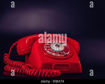 Téléphone rouge vintage à cadran avec câble spiralé photographié sur un fond sombre avec un espace de copie généreux. Banque D'Images