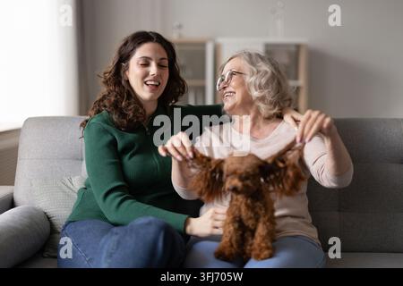 Grand-mère âgée et jeune adulte petite-fille jouant avec un chien à la maison Banque D'Images