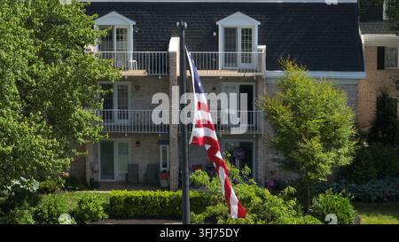 Vue panoramique d'un drapeau américain flottant doucement dans la brise dans une cour devant un complexe d'appartements par une journée d'été claire, Willow Street Banque D'Images
