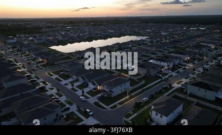 Nouvelle zone résidentielle avec des maisons modernes à deux étages et un petit lac au centre du quartier. Lever du soleil et conduite de voiture sur la rue. Vue aérienne large Banque D'Images