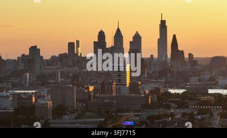 Silhouette de la skyline de Philadelphie à un coucher de soleil doré. Plan large en montée aérienne. Centre-ville avec des gratte-ciel en Amérique. Voitures sur la route en banlieue Banque D'Images