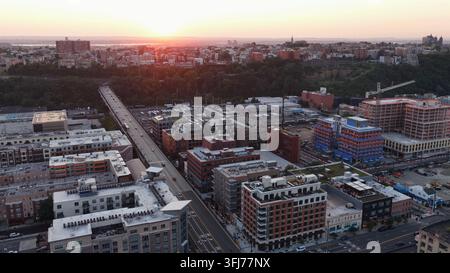 La ligne d'horizon du centre-ville de Hoboken brille au coucher du soleil avec des bâtiments en briques mélangées, une grue de construction domine un nouveau gratte-ciel à côté d'un pont autoroutier surélevé Banque D'Images