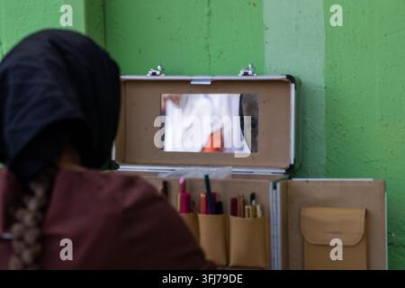 Maquilleur ou artiste se préparant avec une trousse de maquillage ouverte tout en regardant dans un petit miroir, un œil étant reflété dans le verre. Beauté créative Banque D'Images