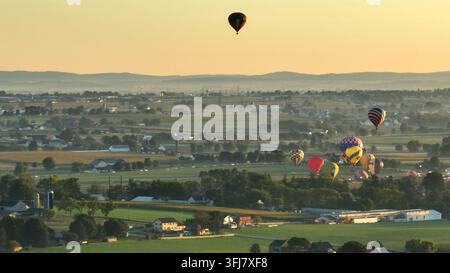 Plan large aérien montrant de nombreux ballons à air chaud décollant sur un champ verdoyant dans la campagne américaine au lever du soleil, East Lampeter Township, Pennsylvanie Banque D'Images