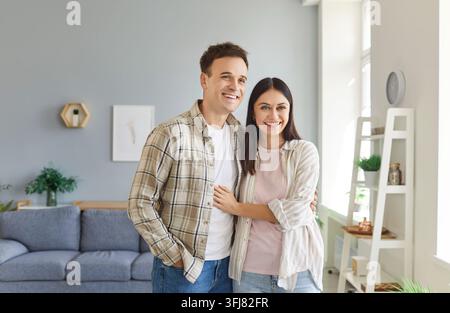 Portrait d'un jeune couple heureux et souriant debout ensemble dans le salon à la maison et s'embrassant. Banque D'Images