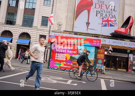 Les cyclistes passent devant un kiosque touristique et l'extérieur du Dominion Theatre sur Tottenham Court Road où Le Diable porte Prada est actuellement joué, le 18 septembre 2026, à Londres, en Angleterre. Banque D'Images
