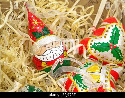 Vue rapprochée de décorations de Noël colorées peintes à la main, comprenant une figurine du Père Noël et des ornements en forme d'étoile reposant dans un emballage en paille déchiré Banque D'Images