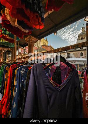 Des robes flamenco vibrantes sont accrochées à un étalage d'une boutique sur la place centrale Pan de Séville, avec le clocher historique de l'église Salvador visible dans le fond ensoleillé Banque D'Images