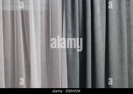 Close-up de rideaux superposés présentant un tissu blanc transparent à côté d'une draperie en velours gris texturé riche, baignée d'une lumière naturelle douce. Banque D'Images