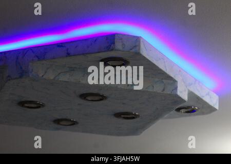 Élément de plafond texturé moderne avec spots encastrés et bande lumineuse LED bleu-violet vibrante créant une lueur colorée. Banque D'Images