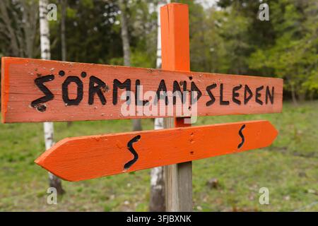 Panneau de sentier en bois orange marquant le sentier de randonnée Sörmlandsleden en Suède. Le panneau porte le nom SÖRMLANDSLEDEN et la forme caractéristique en S Banque D'Images